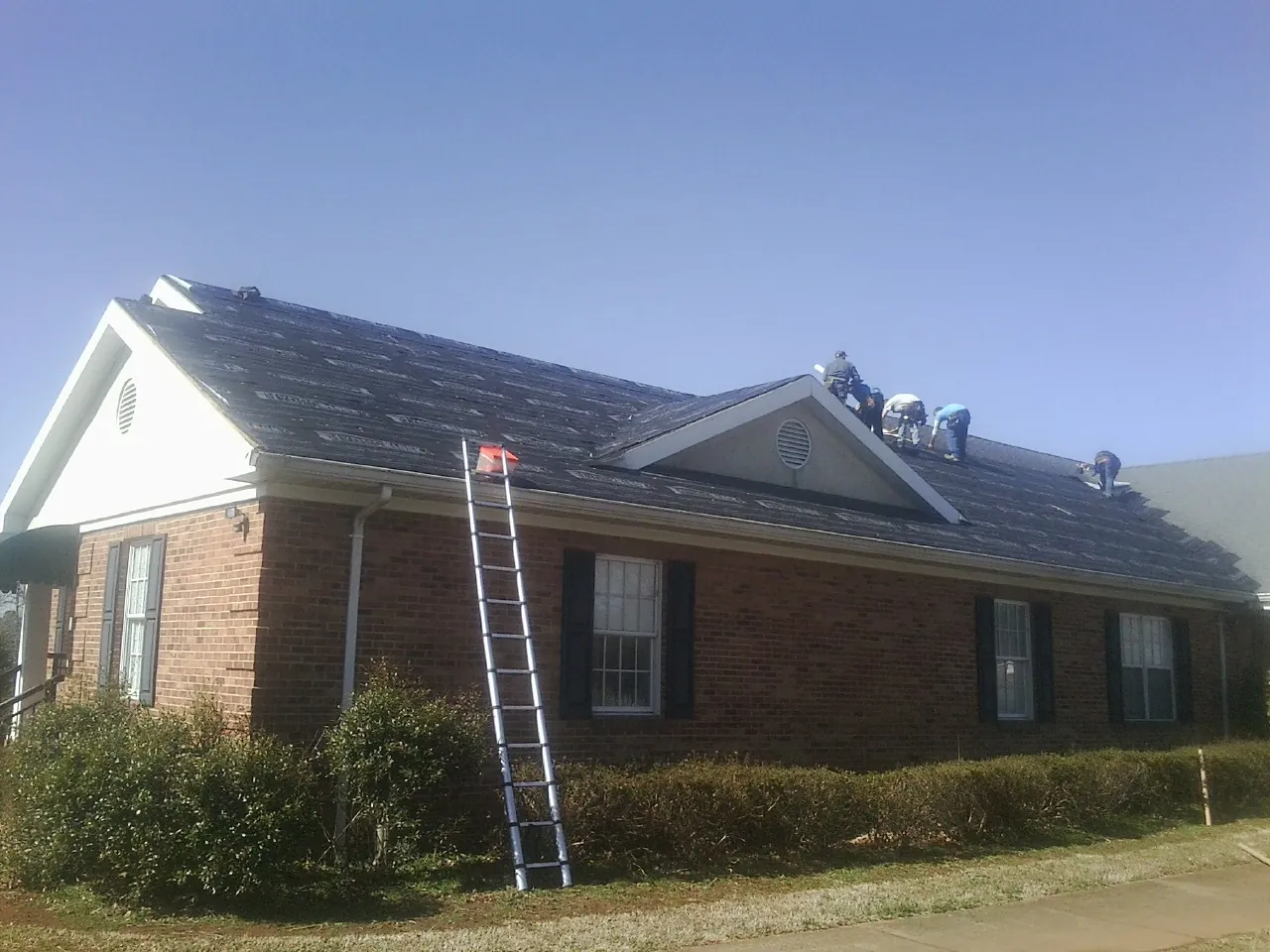 Crew tearing shingles off a brick ranch roof with a ladder set — Metal Roof Repair work by our crew in Franklin Lakes