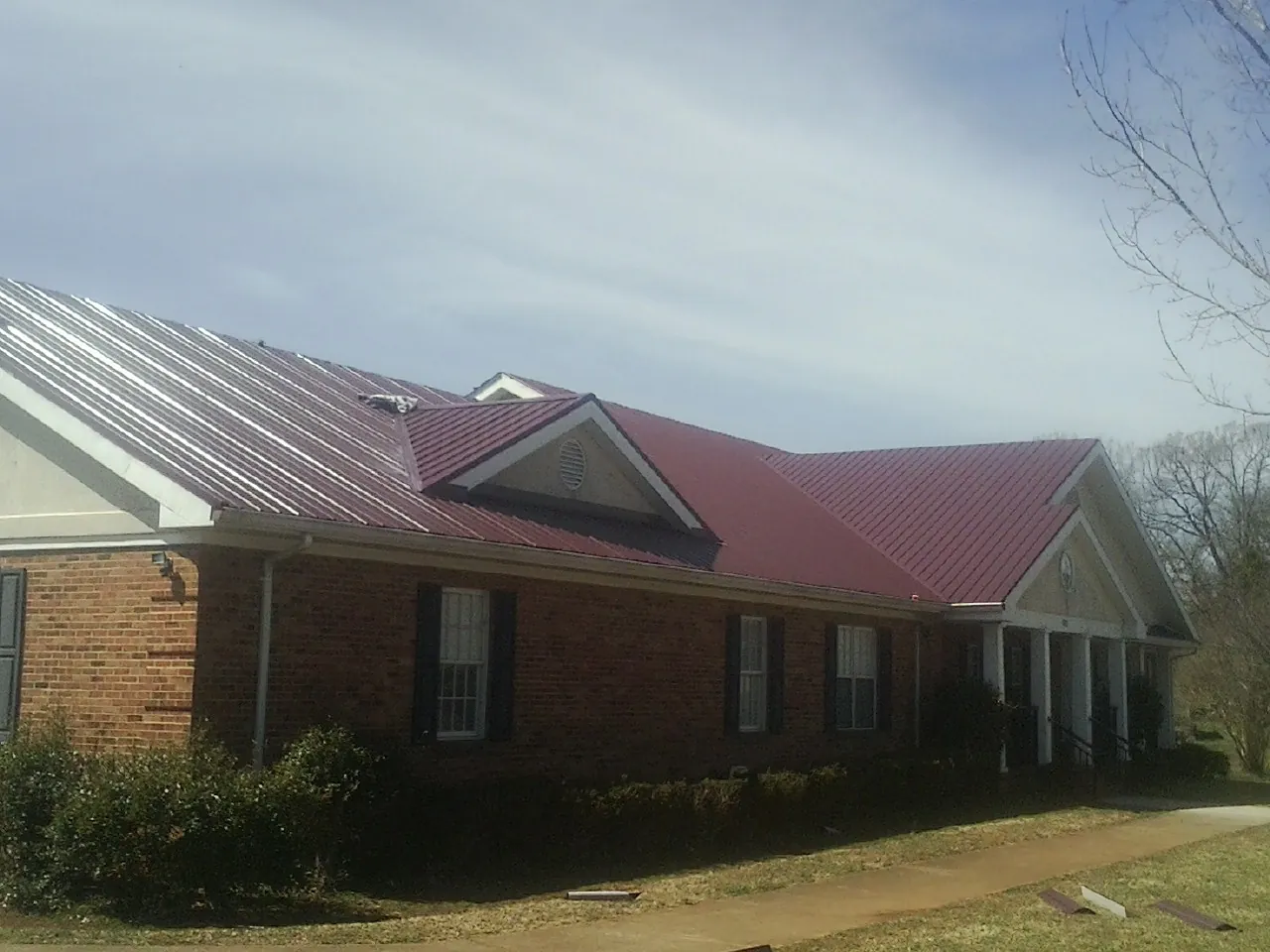 Red metal roof with gabled entries on a long brick building, from a Hail Damage Roof Repair job in Franklin Lakes
