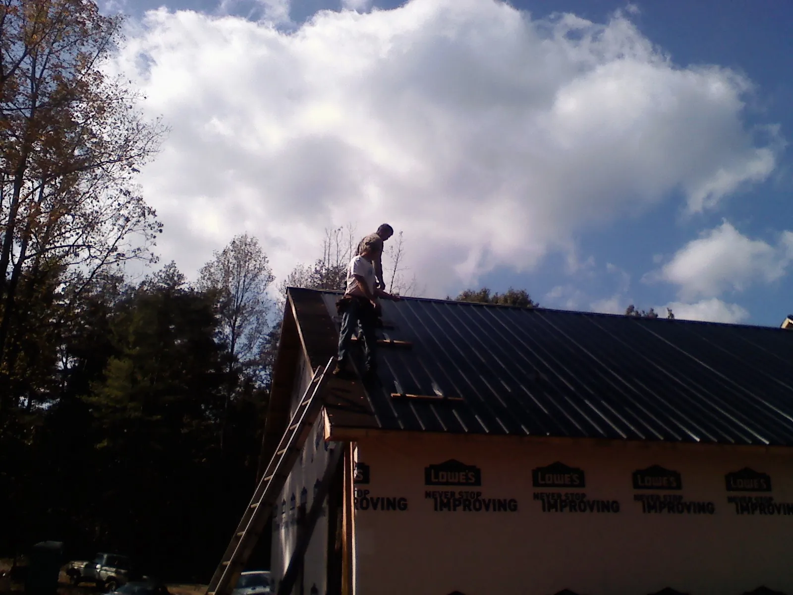 Roofer fastening dark metal panels high against a cloudy sky, from a Roof Inspection job in Franklin Lakes