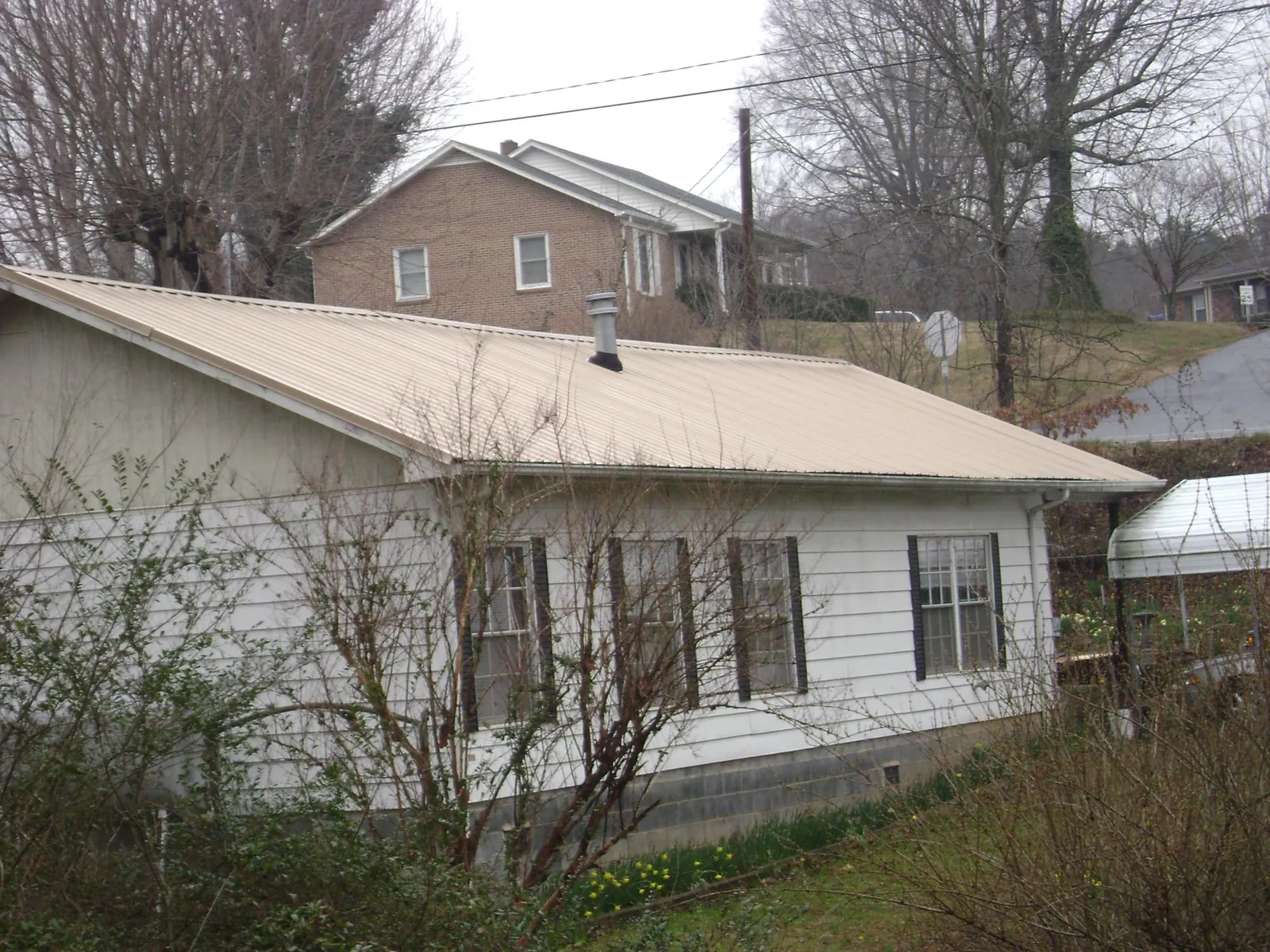 Tan metal roof on a white sided house set into a hillside — Commercial Roofing by Roofing Brothers in Franklin Lakes